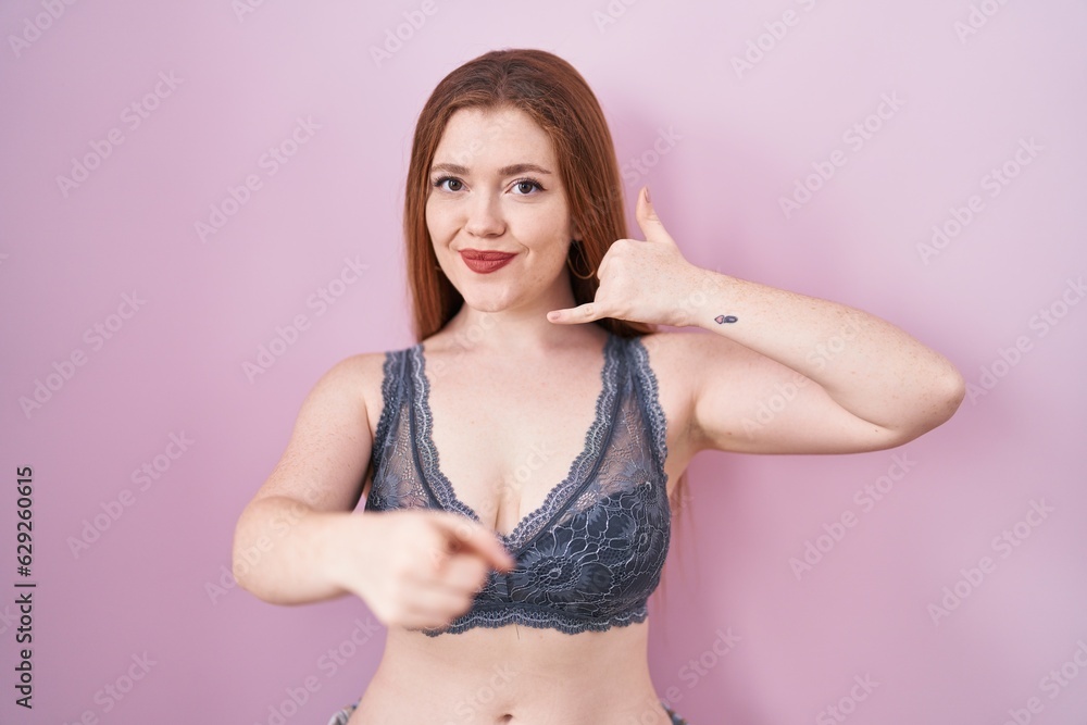 Φωτογραφία Redhead woman wearing lingerie over pink background smiling doing talking on the telephone gesture and pointing to you