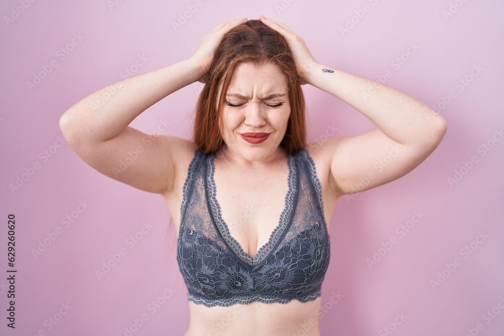 Redhead woman wearing lingerie over pink background suffering from headache desperate and stressed because pain and migraine. hands on head. Redhead woman wearing lingerie over pink background suffering from headache desperate and stressed because pain and migraine. hands on head.