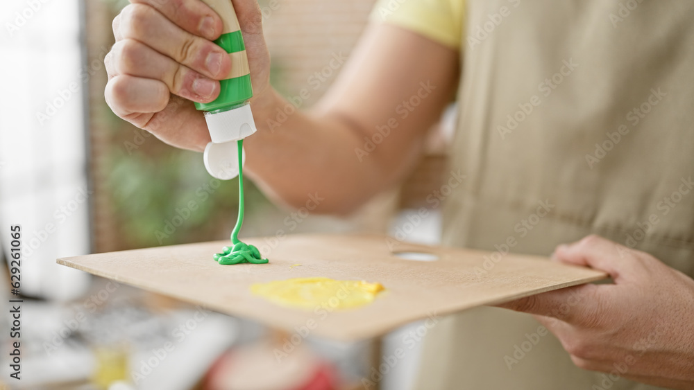 Obraz premium Young hispanic man artist pouring color on palette at art studio
