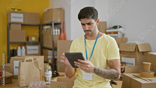 Young hispanic man volunteer using touchpad with serious face at charity center