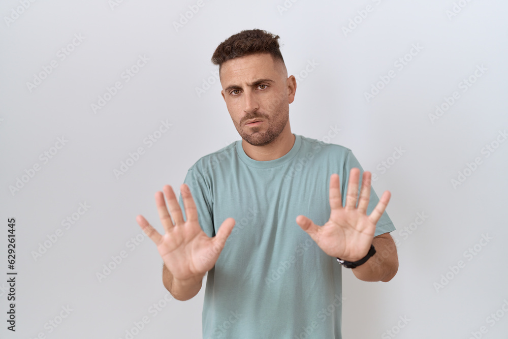 Hispanic man with beard standing over white background moving away hands palms showing refusal and denial with afraid and disgusting expression. stop and forbidden.