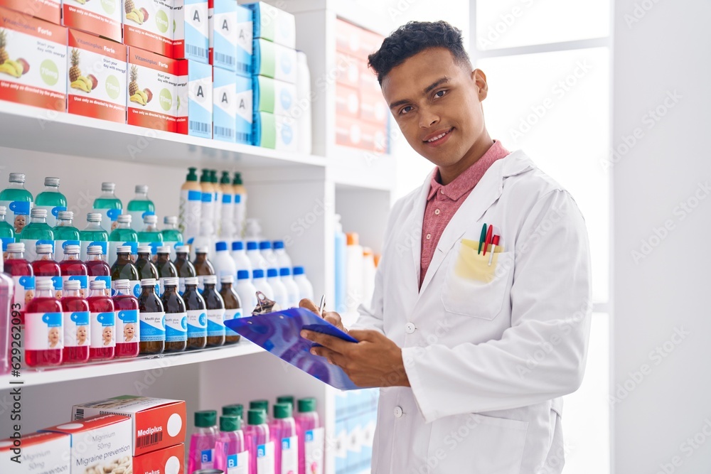 Young latin man pharmacist smiling confident writing report at pharmacy