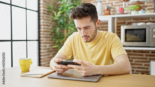 Young hispanic man playing video game sitting on table at dinning room