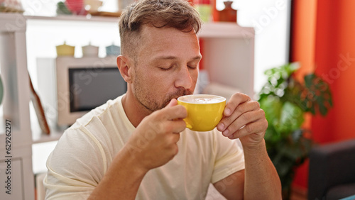 Young man smelling cup of coffee sitting on table at dinning room