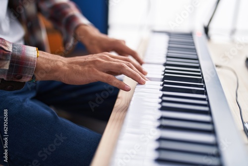 Young hispanic man musician playing piano at music studio