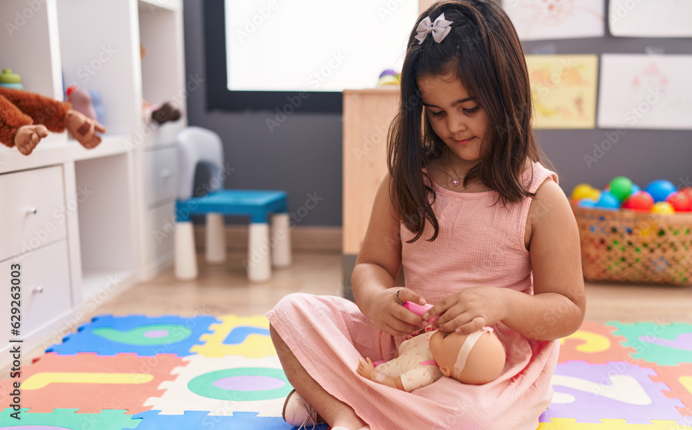 Adorable hispanic girl sitting on floor playing with baby doll at kindergarten Adorable hispanic girl sitting on floor playing with baby doll at kindergarten