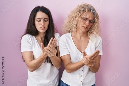 Mother and daughter standing together over pink background suffering pain on hands and fingers, arthritis inflammation