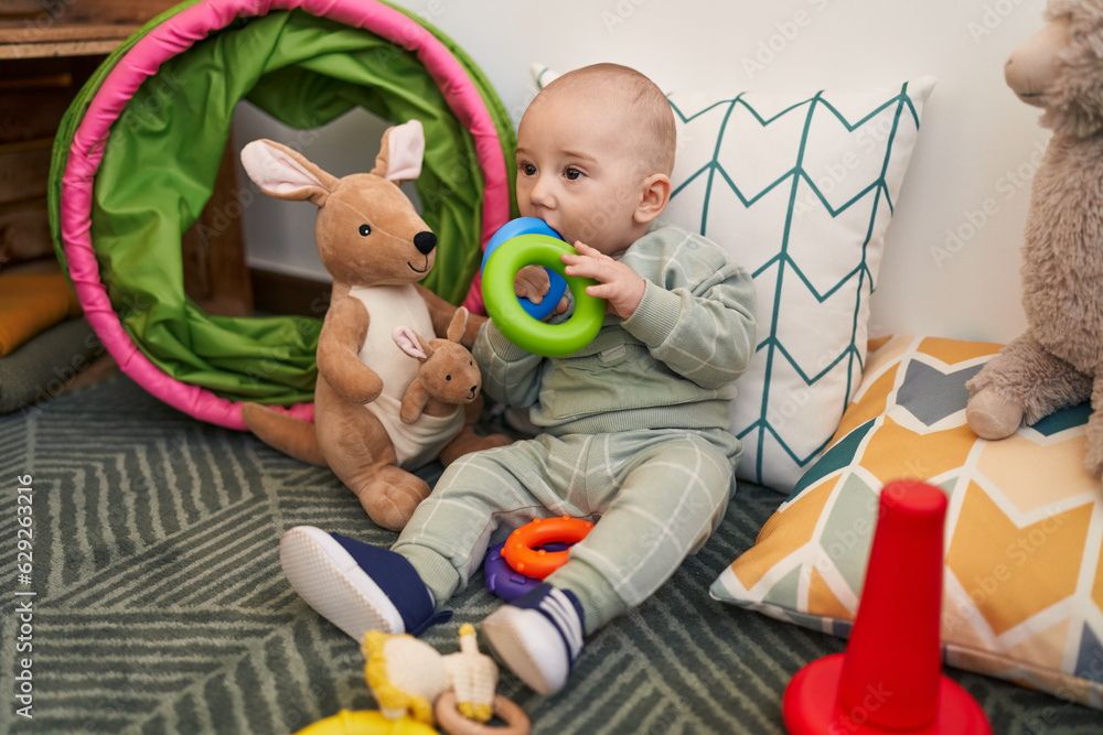 Naklejka premium Adorable caucasian baby sitting on floor sucking hoops at home