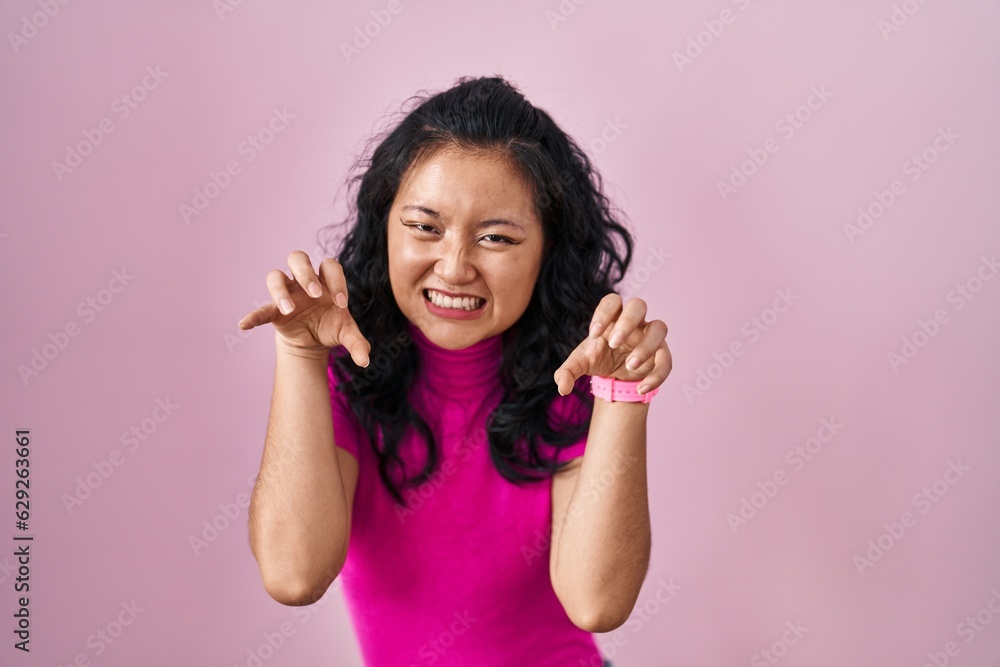 Young asian woman standing over pink background smiling funny doing claw gesture as cat, aggressive and sexy expression Young asian woman standing over pink background smiling funny doing claw gesture as cat, aggressive and sexy expression