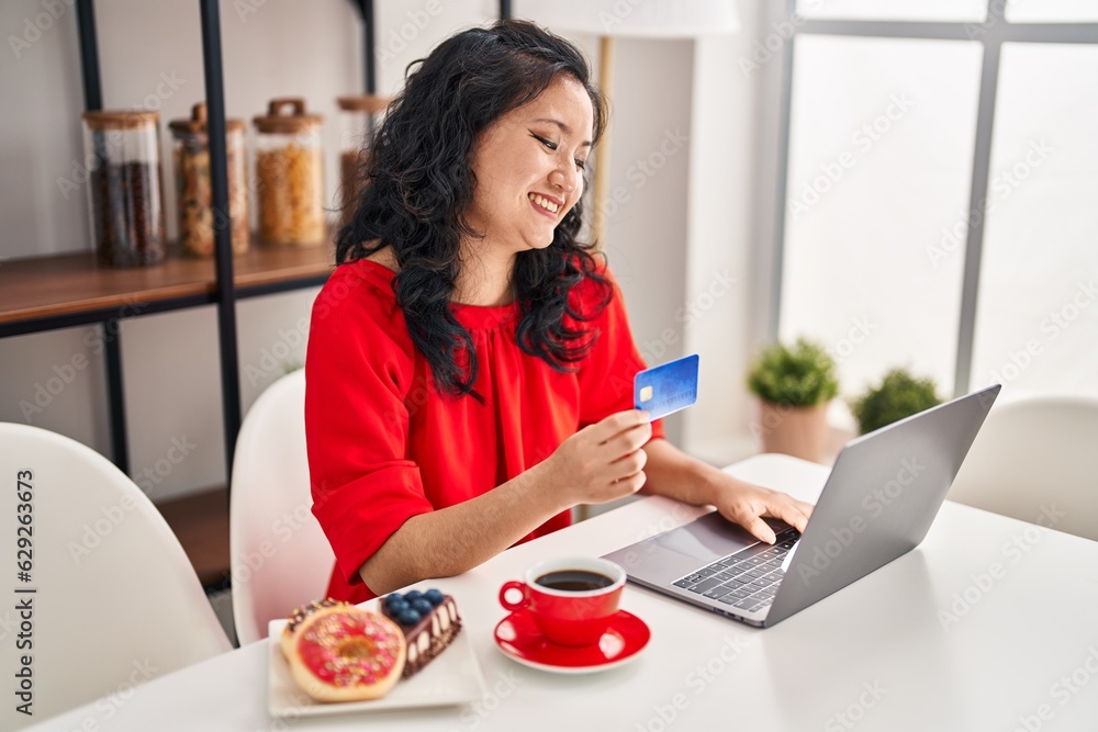 Young chinese woman having breakfast using laptop and credit card at home Young chinese woman having breakfast using laptop and credit card at home