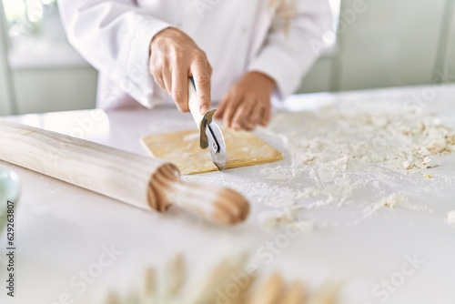 Young woman wearing cook uniform cutting pasta dough at kitchen