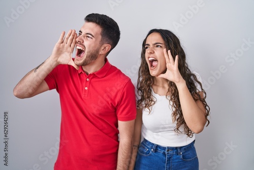 Young hispanic couple standing over isolated background shouting and screaming loud to side with hand on mouth. communication concept.
