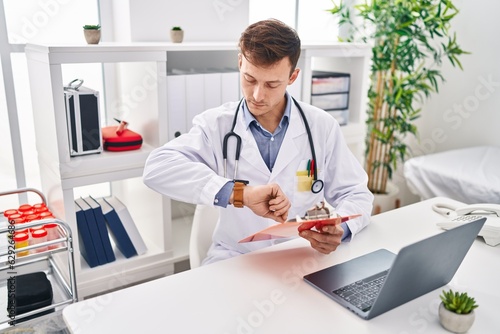 Young man doctor reading report looking watch at clinic