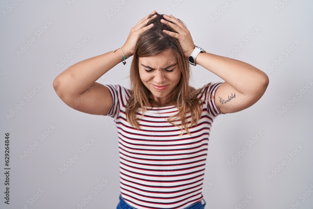 Young hispanic woman standing over isolated background suffering from headache desperate and stressed because pain and migraine. hands on head. Young hispanic woman standing over isolated background suffering from headache desperate and stressed because pain and migraine. hands on head.