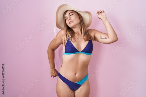 Young hispanic woman wearing bikini over pink background stretching back, tired and relaxed, sleepy and yawning for early morning