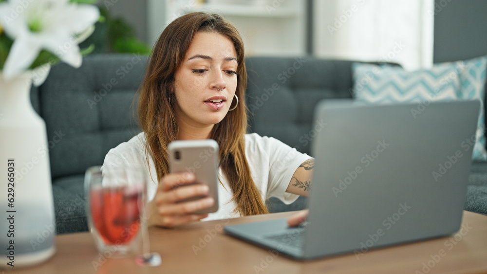 Young beautiful hispanic woman using laptop and smartphone sitting on floor at home Young beautiful hispanic woman using laptop and smartphone sitting on floor at home