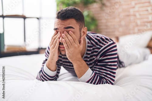 Young hispanic man stressed lying on bed at bedroom