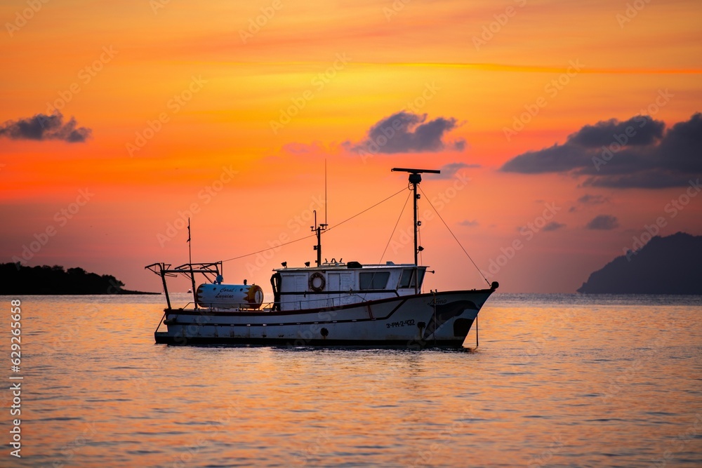 Large fishing boat is silhouetted against a stunning sunset