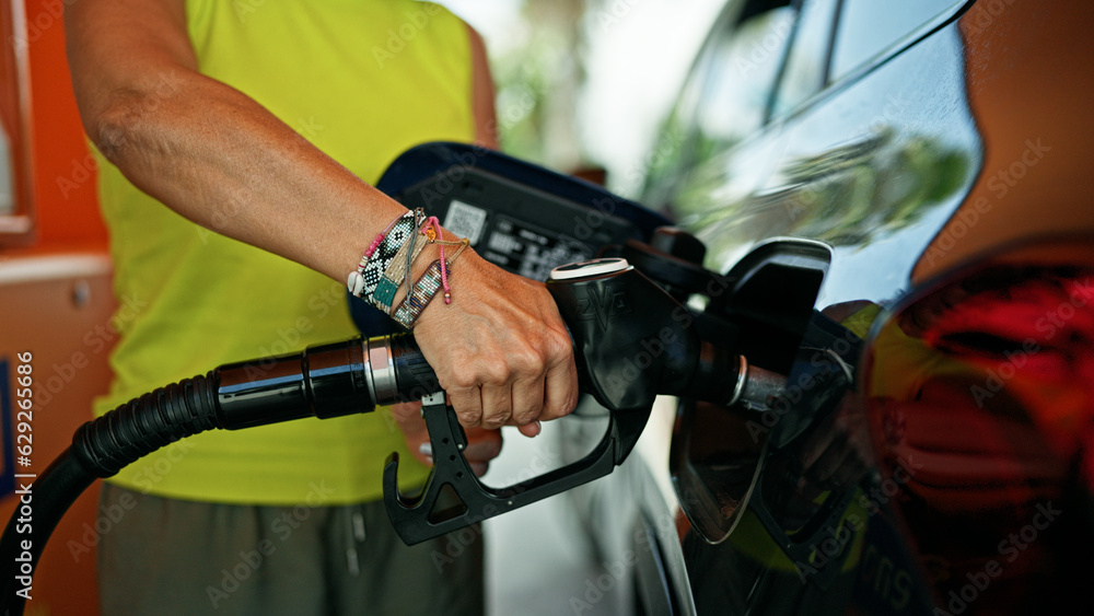 Middle age hispanic woman putting gas in the car at gas station Middle age hispanic woman putting gas in the car at gas station