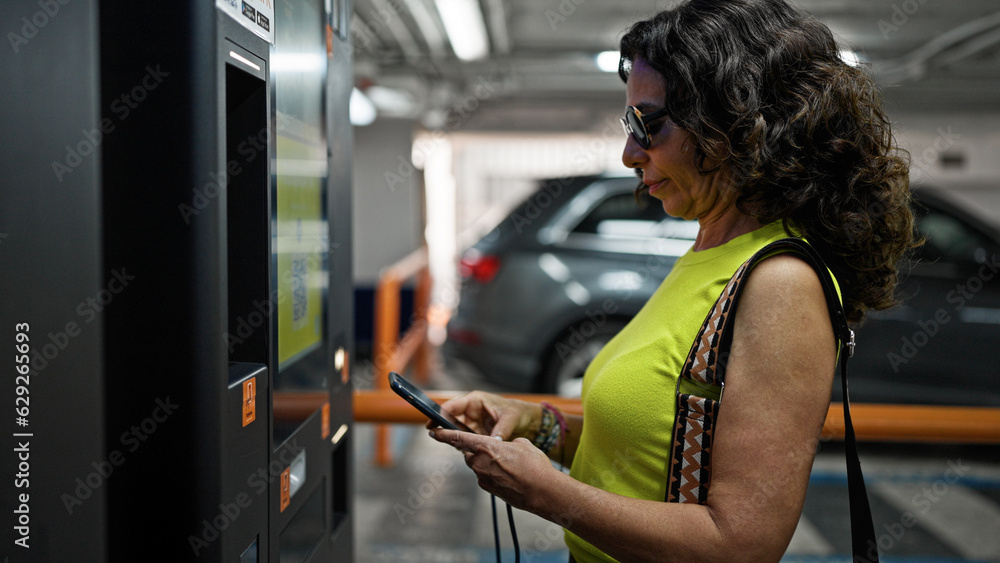 Middle age hispanic woman paying at parking machine parking