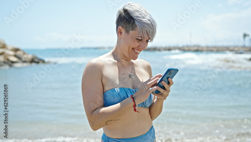Young woman tourist wearing bikini using smartphone smiling at beach