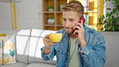 Young caucasian man talking on smartphone drinking coffee at home
