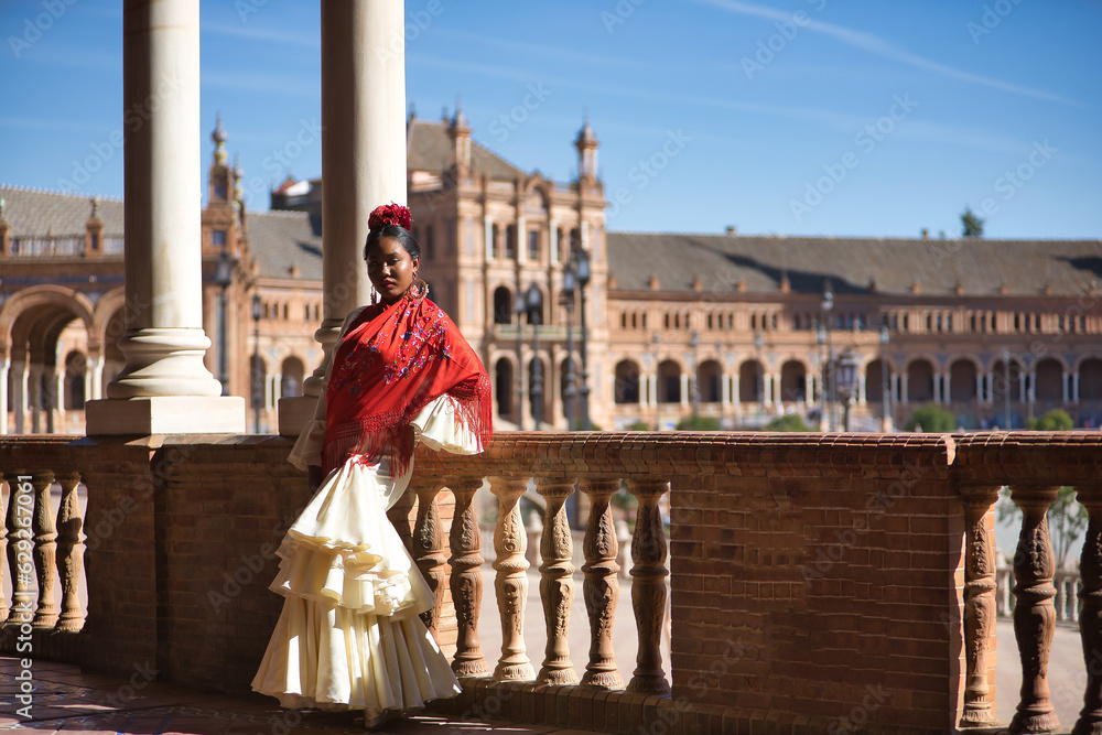Young black and South American woman in a beige gypsy flamenco suit, posing in a beautiful square in the city of Seville in Spain. Concept dance, folklore, flamenco, art.