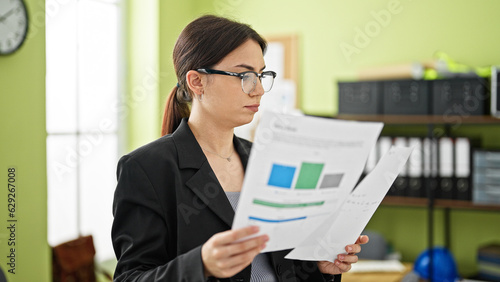 Young beautiful hispanic woman business worker reading document with serious face at office