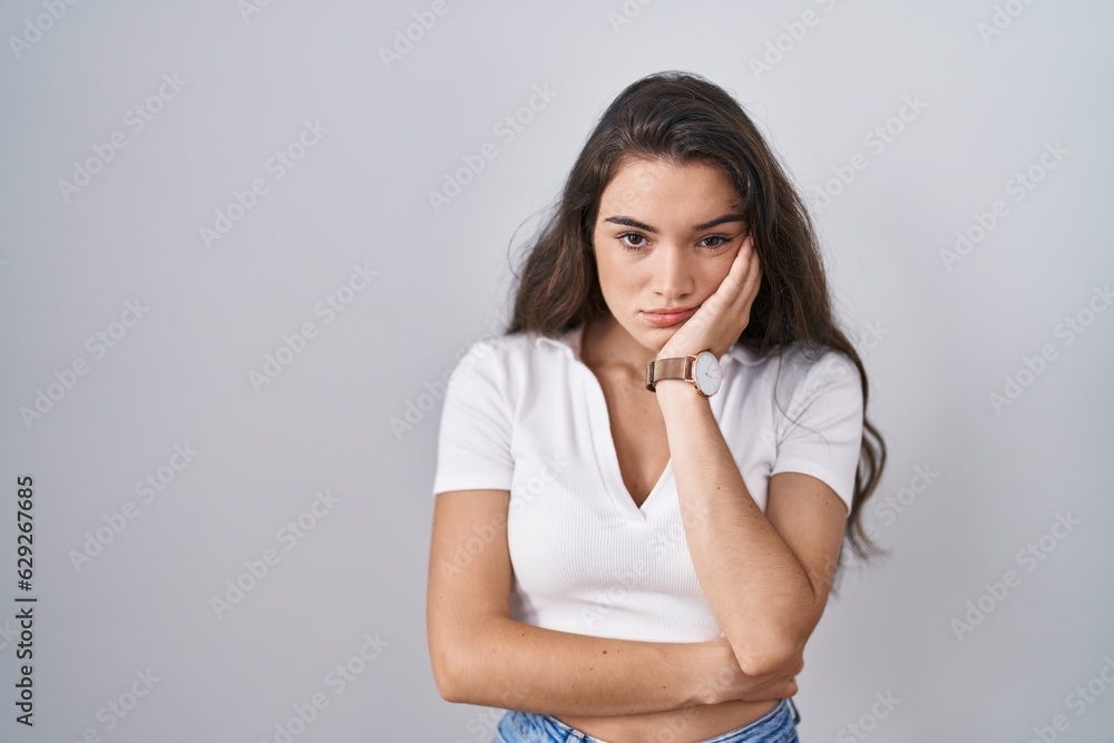 Young teenager girl standing over white background thinking looking tired and bored with depression problems with crossed arms.