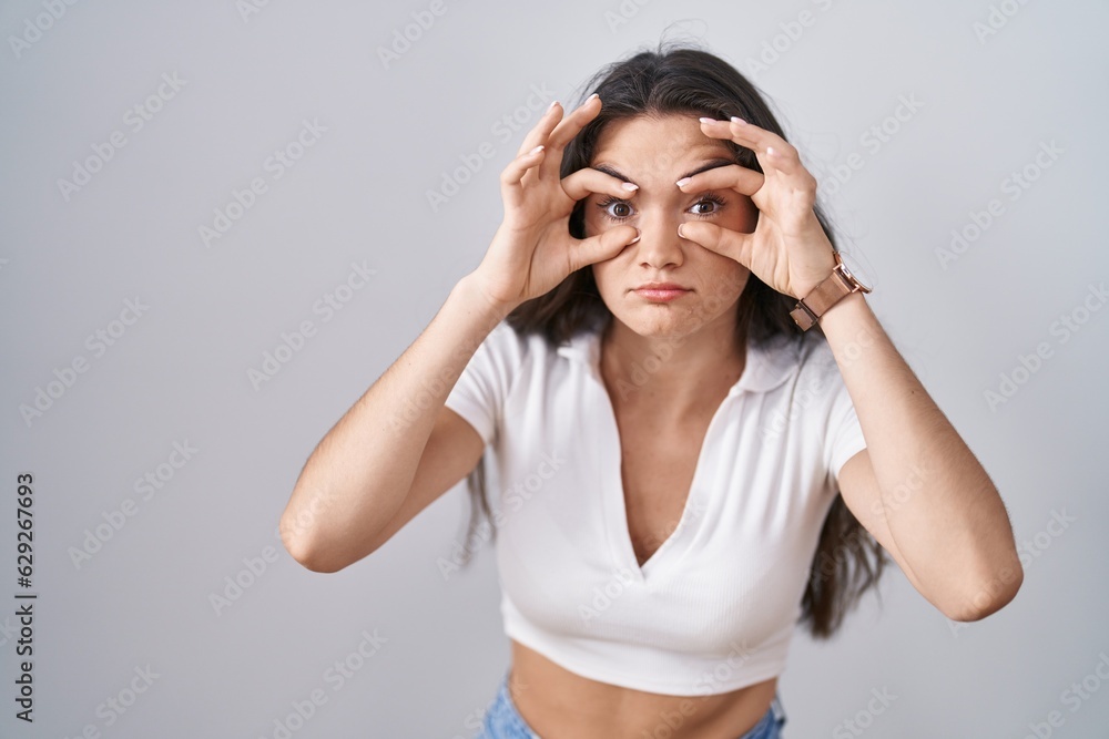 Young teenager girl standing over white background trying to open eyes with fingers, sleepy and tired for morning fatigue Young teenager girl standing over white background trying to open eyes with fingers, sleepy and tired for morning fatigue