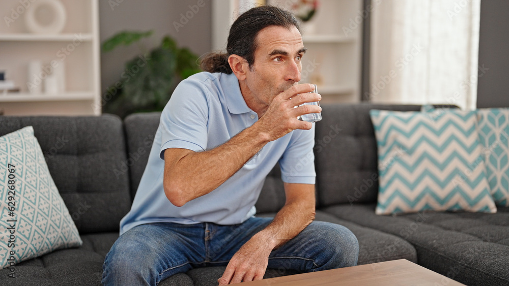 Middle age man drinking glass of water sitting on sofa at home