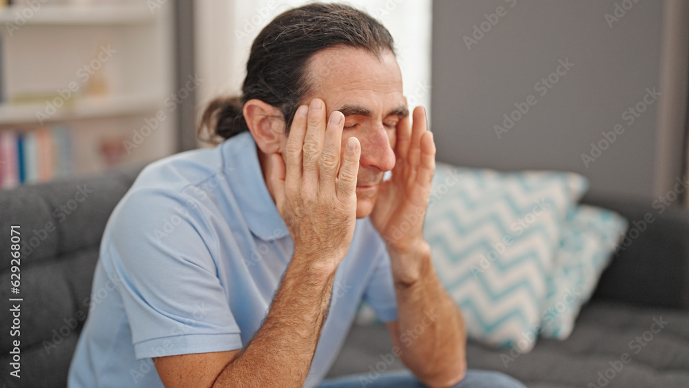 Middle age man suffering for headache sitting on sofa at home Middle age man suffering for headache sitting on sofa at home