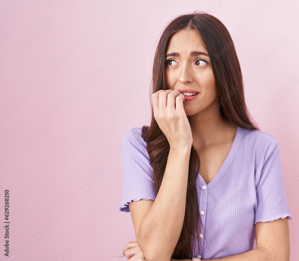 Young hispanic woman with long hair standing over pink background looking stressed and nervous with hands on mouth biting nails. anxiety problem. Young hispanic woman with long hair standing over pink background looking stressed and nervous with hands on mouth biting nails. anxiety problem.