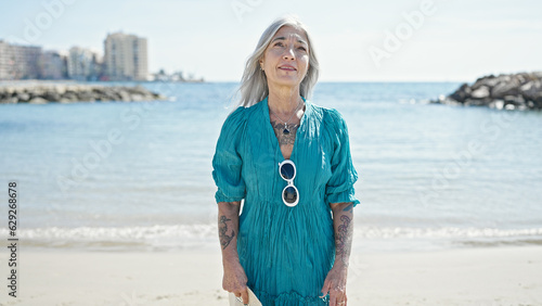 Middle age grey-haired woman standing with relaxed expression at beach