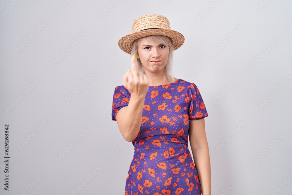 Young caucasian woman wearing flowers dress and summer hat showing middle finger, impolite and rude fuck off expression Young caucasian woman wearing flowers dress and summer hat showing middle finger, impolite and rude fuck off expression