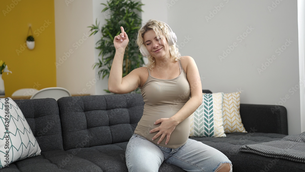 Obraz premium Young pregnant woman listening to music touching belly and dancing at home