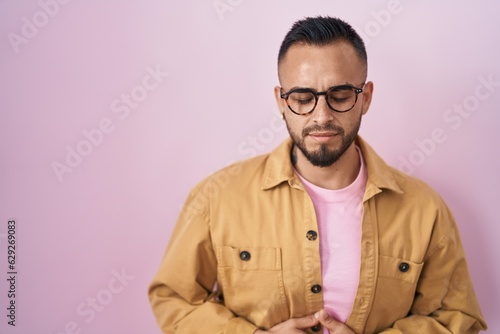 Young hispanic man standing over pink background with hand on stomach because indigestion, painful illness feeling unwell. ache concept. © Krakenimages.com