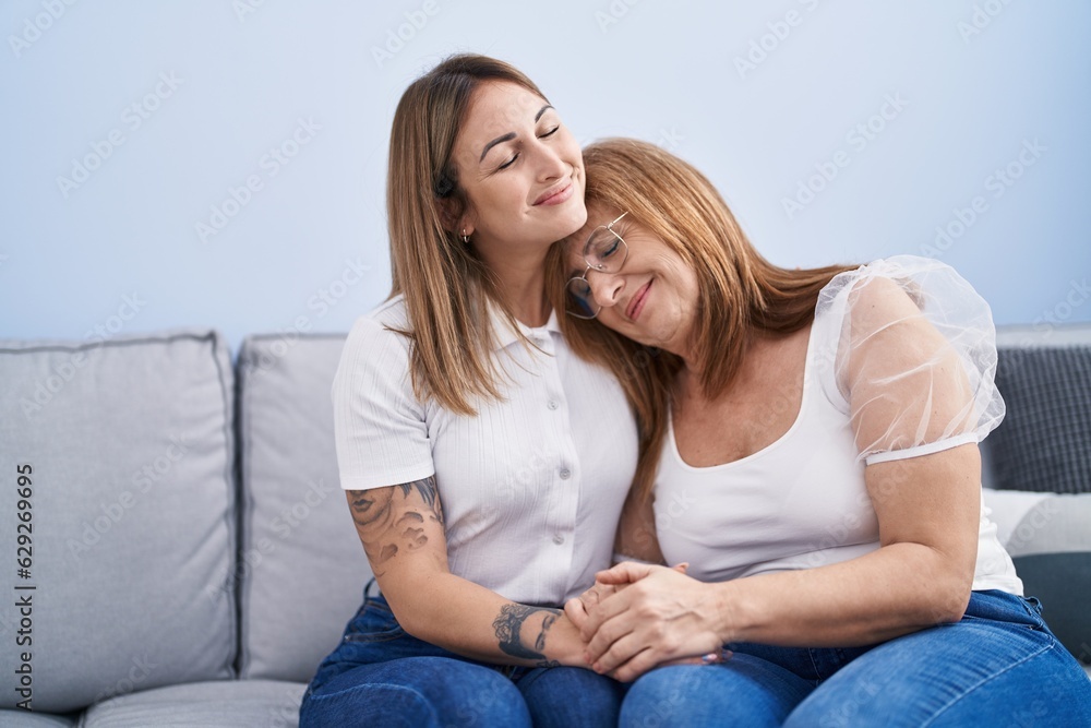 Mother and daughter hugging each other sitting on sofa at home