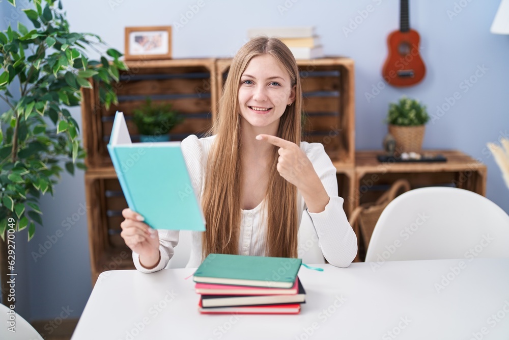 Young caucasian woman reading books at home smiling happy pointing with hand and finger Young caucasian woman reading books at home smiling happy pointing with hand and finger