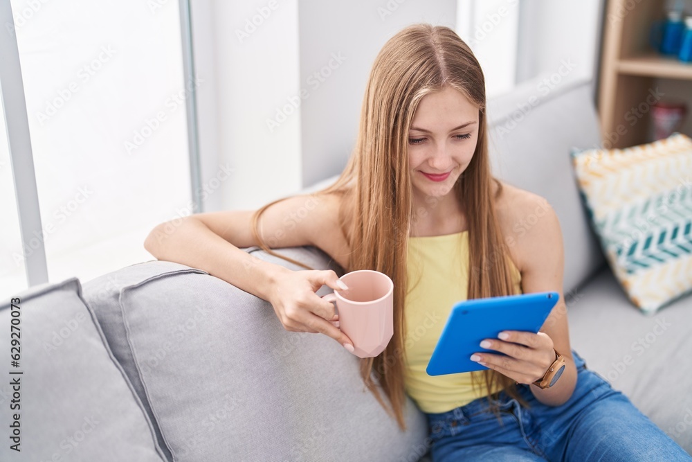 Young caucasian woman drinking coffee using touchpad at home Young caucasian woman drinking coffee using touchpad at home