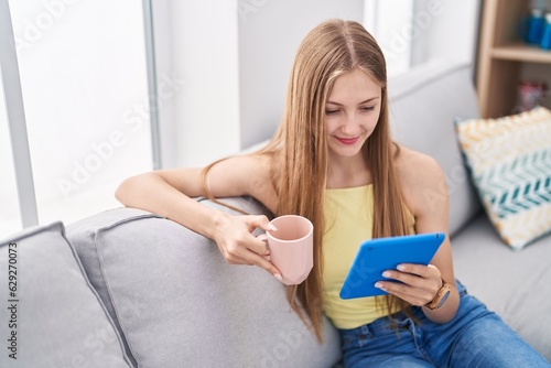 Young caucasian woman drinking coffee using touchpad at home