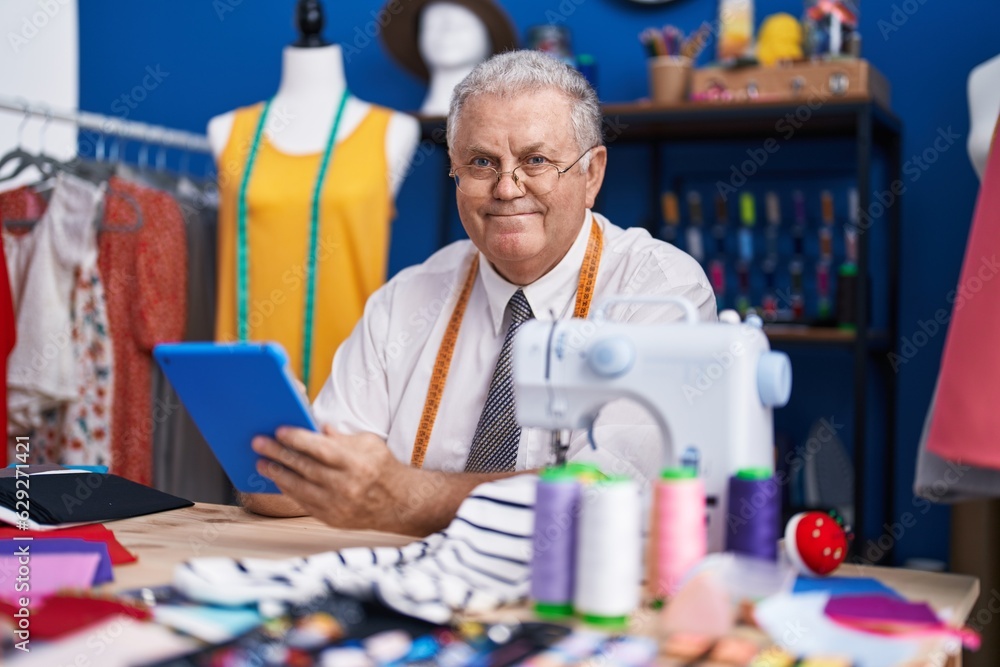 Middle age grey-haired man tailor smiling confident using touchpad at tailor shop Middle age grey-haired man tailor smiling confident using touchpad at tailor shop