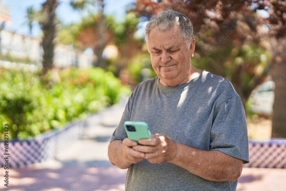 Fototapeta premium Middle age grey-haired man using smartphone with relaxed expression at park