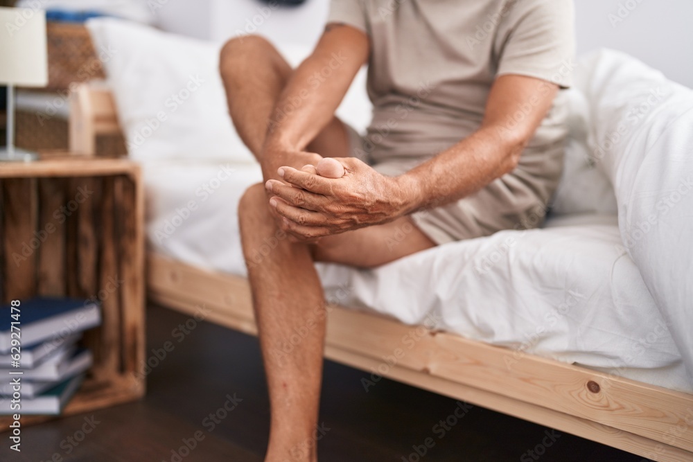 Middle age man suffering for feet pain sitting on bed at bedroom