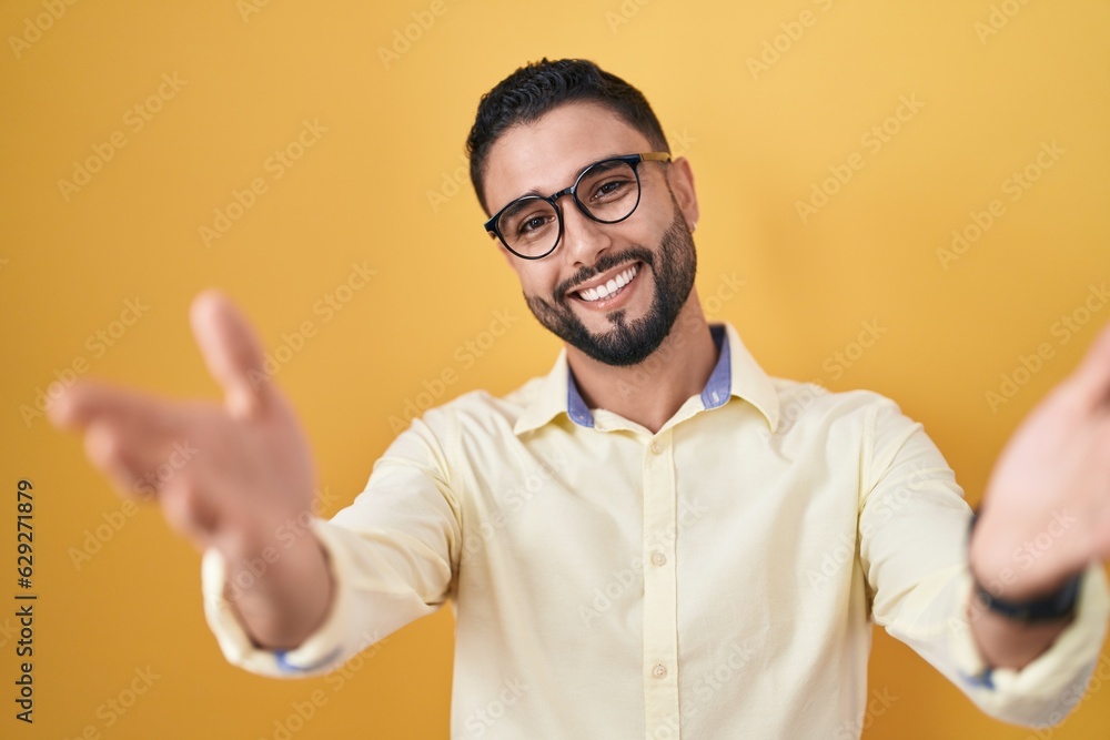 Hispanic young man wearing business clothes and glasses smiling cheerful offering hands giving assistance and acceptance. Hispanic young man wearing business clothes and glasses smiling cheerful offering hands giving assistance and acceptance.