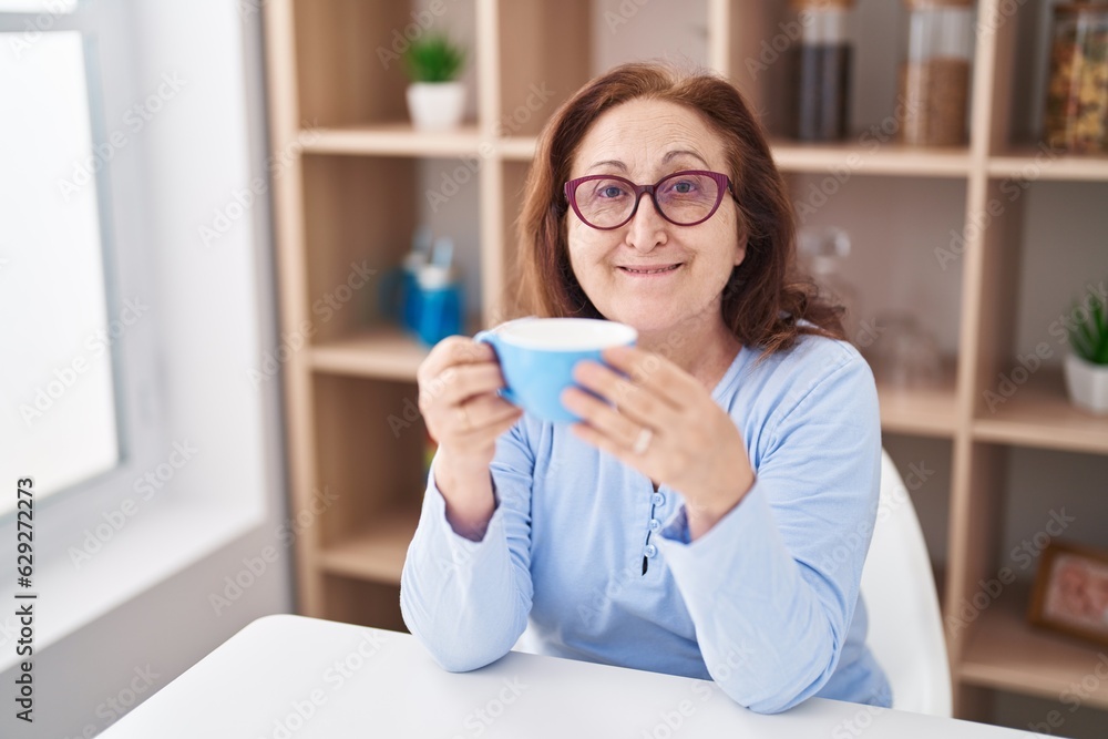 Senior woman drinking coffee sitting on table at home