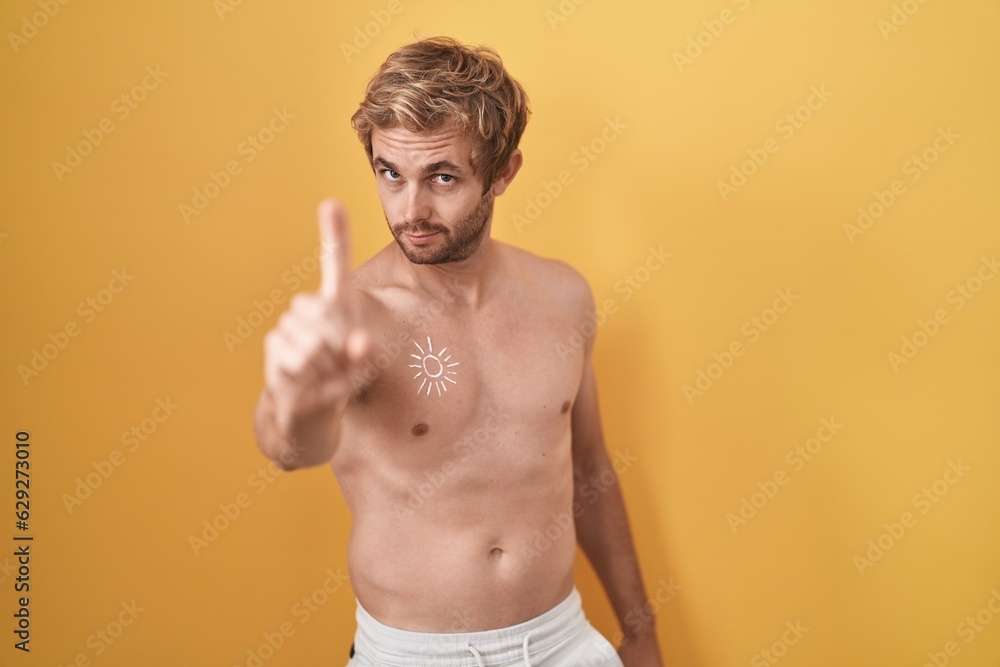 Caucasian man standing shirtless wearing sun screen pointing with finger up and angry expression, showing no gesture