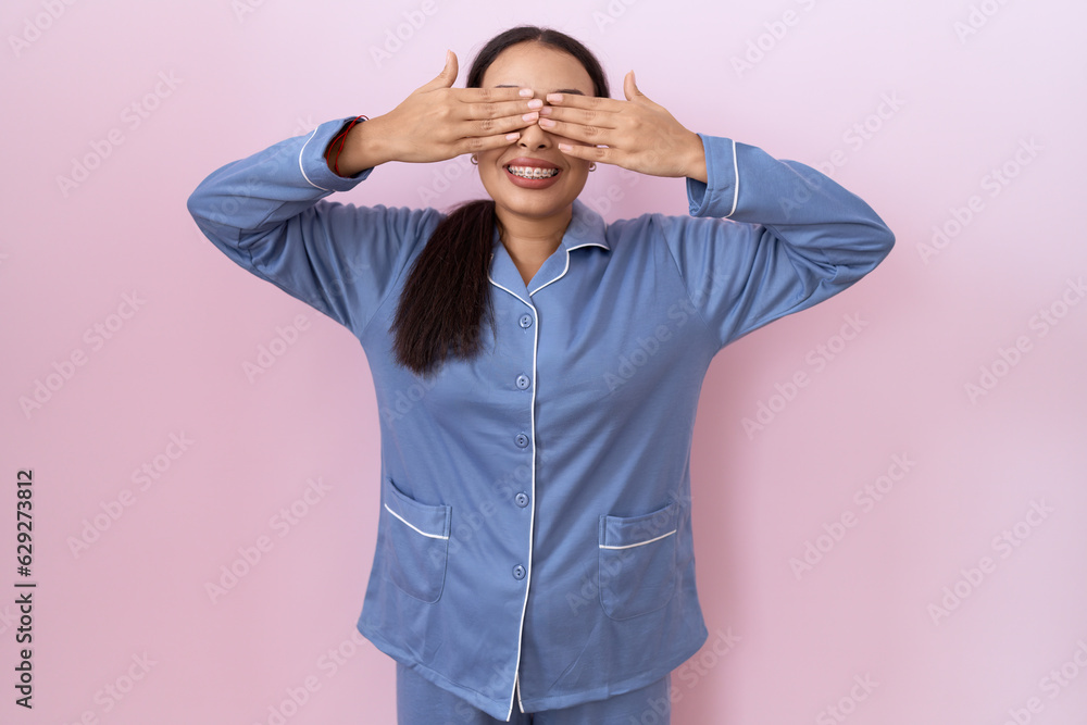 Young arab woman wearing blue pajama covering eyes with hands smiling cheerful and funny. blind concept. Young arab woman wearing blue pajama covering eyes with hands smiling cheerful and funny. blind concept.