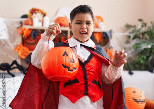 Adorable hispanic boy wearing halloween costume doing scary gesture at home