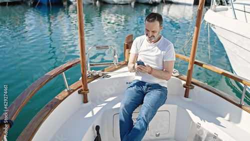 Middle age man using smartphone sitting on boat at port © Krakenimages.com